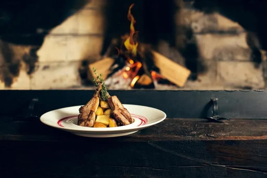 Grilled lamb chops with potatoes served on a white plate near a roaring fireplace, Vipava.