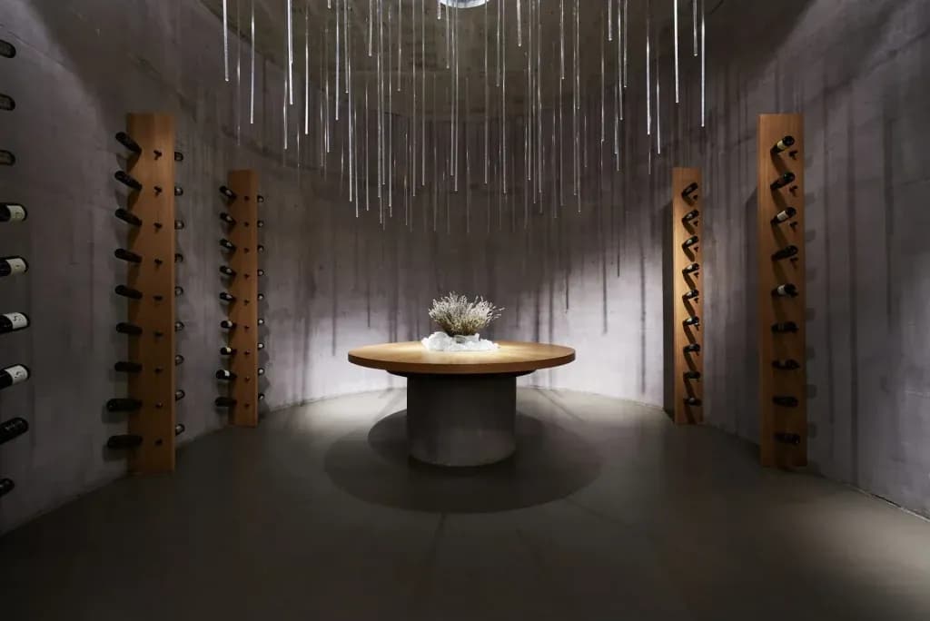 Modern wine cellar with wooden racks, concrete walls, and unique hanging light fixture over a round table.