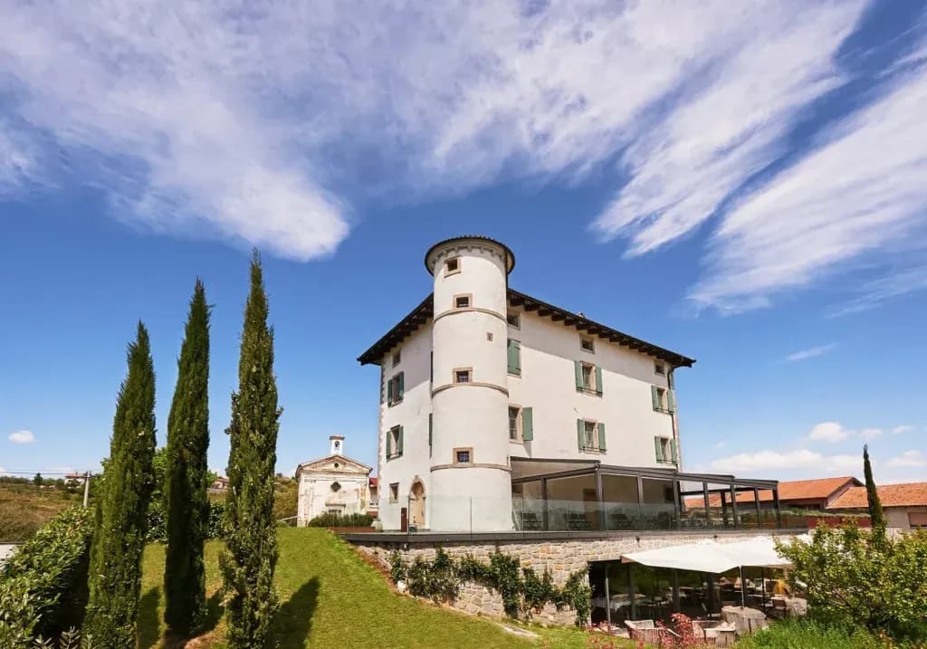 White historic building with a round tower, cypress trees, and blue sky.