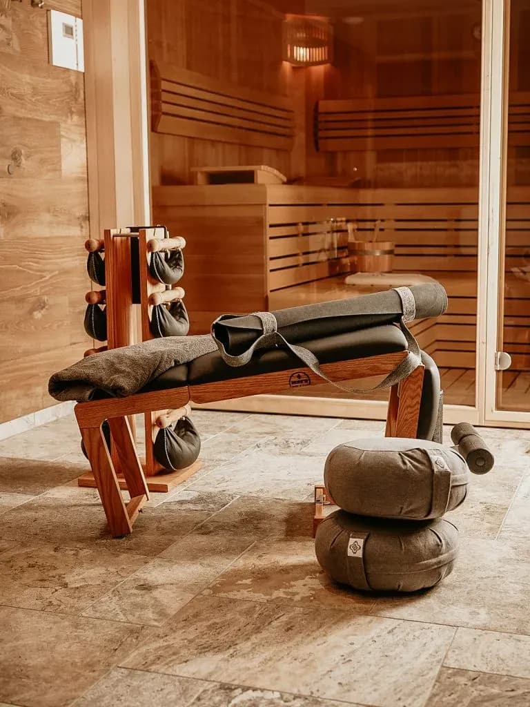 Wooden workout bench, yoga mats, and meditation cushions outside a sauna room.