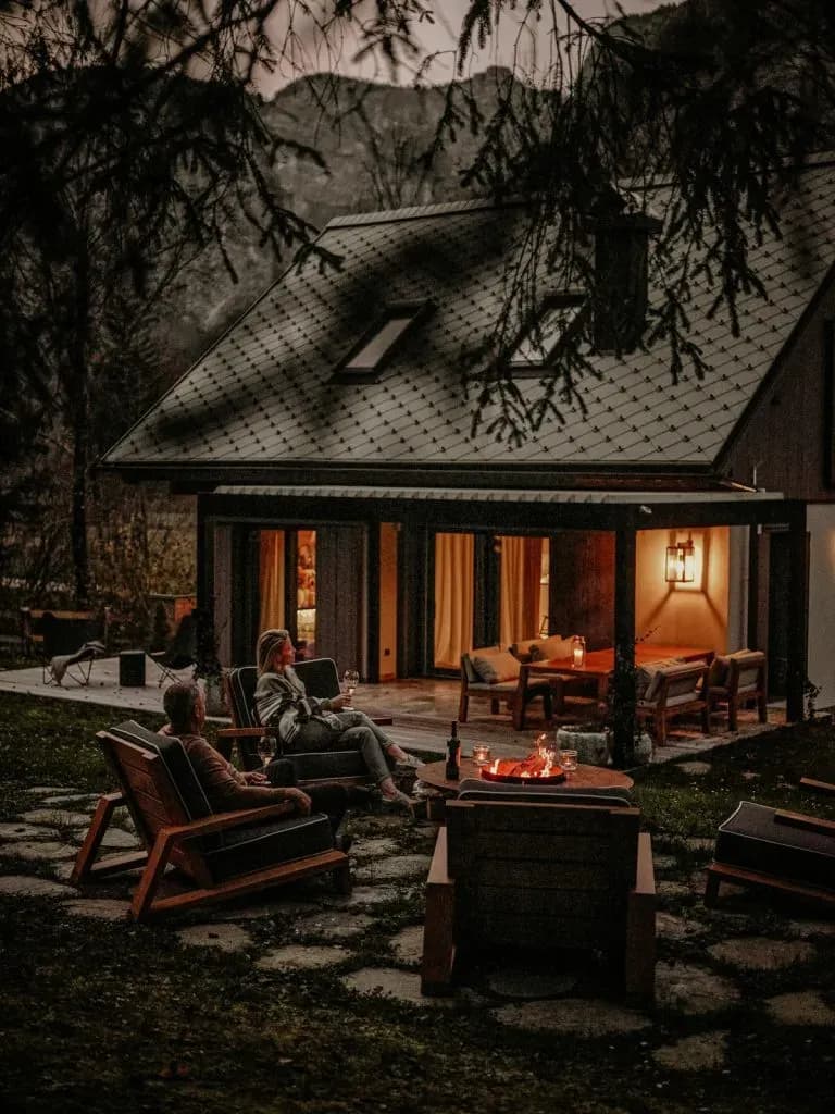 Couple relaxing by fire pit outside modern cabin with mountain backdrop at dusk