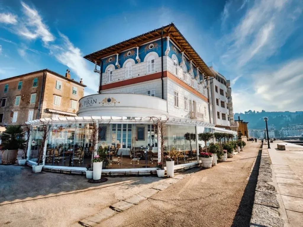 Hotel Piran with glassed-in dining area on waterfront promenade under blue sky