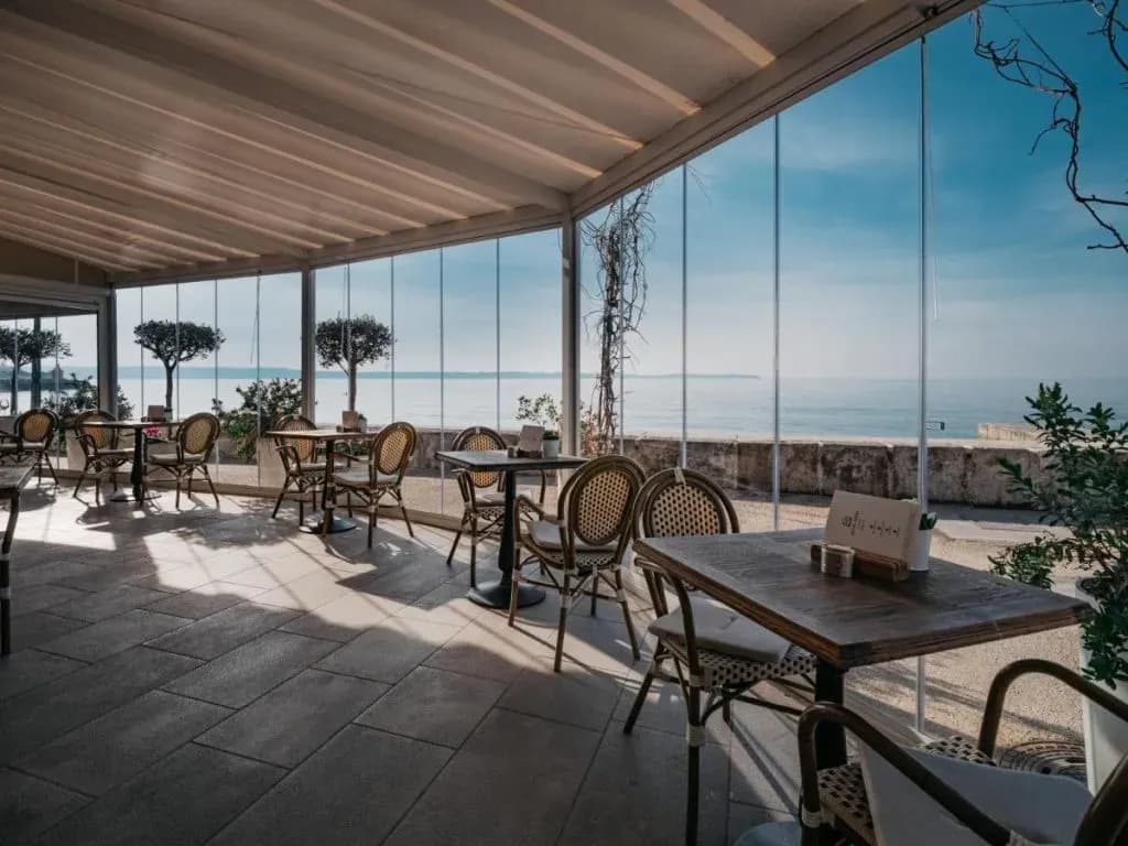 Dining area with wicker chairs overlooking the sea through glass walls at Hotel Piran.