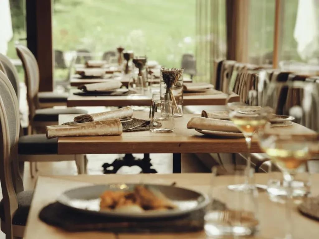 Restaurant dining room with set wooden tables overlooking a green outdoor area