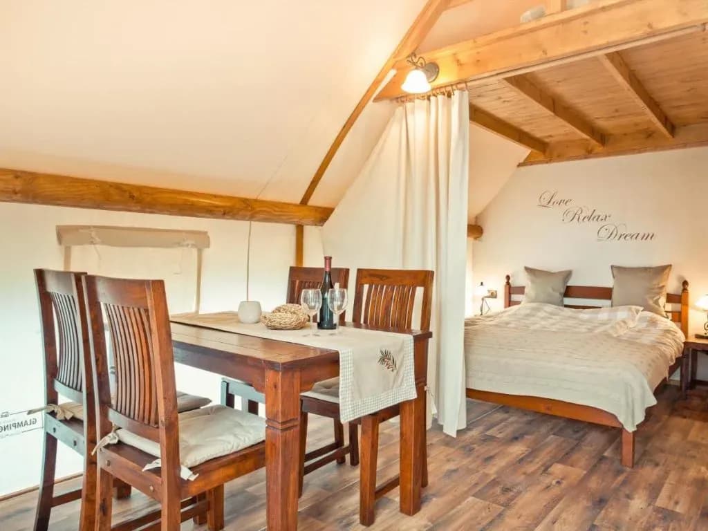 Interior view of rustic glamping tent with wooden dining set and curtained bedroom area