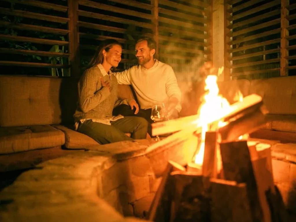 Couple relaxing by outdoor fire pit at night in wooden structure, Ogenj.
