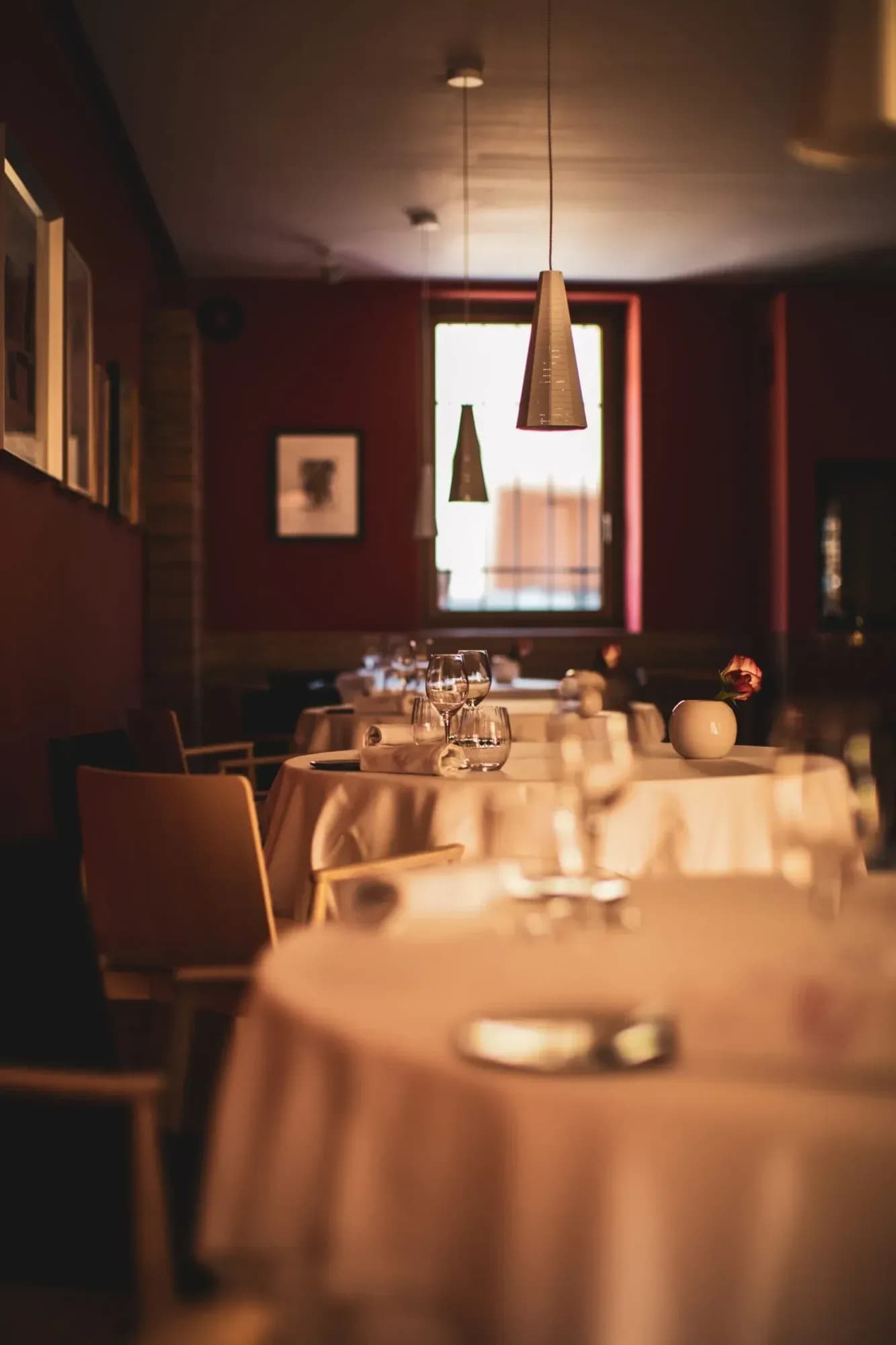 Dining tables set with white linens, wine glasses, and a single rose in a Franko restaurant.