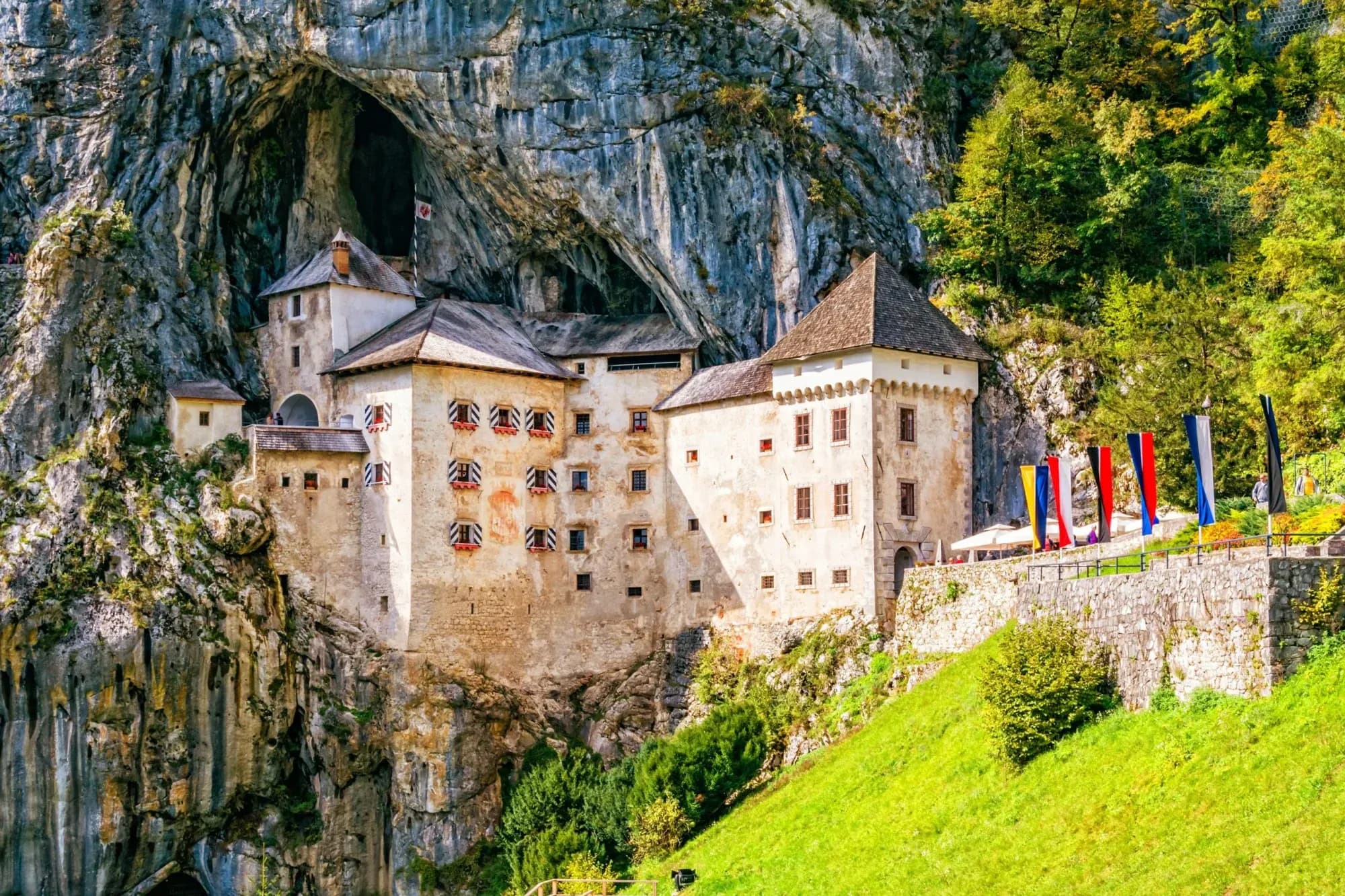 Predjama Castle built into a cliff face with green hillside and colorful flags