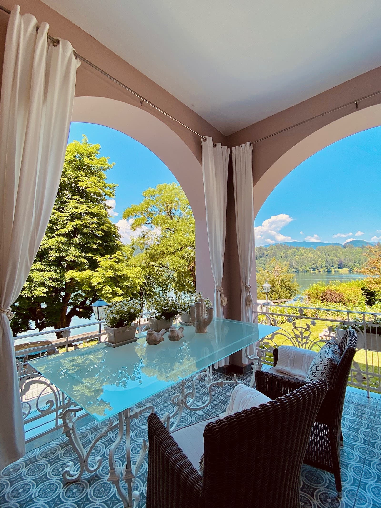 Balcony with glass table overlooking lake and forested mountains on a sunny day