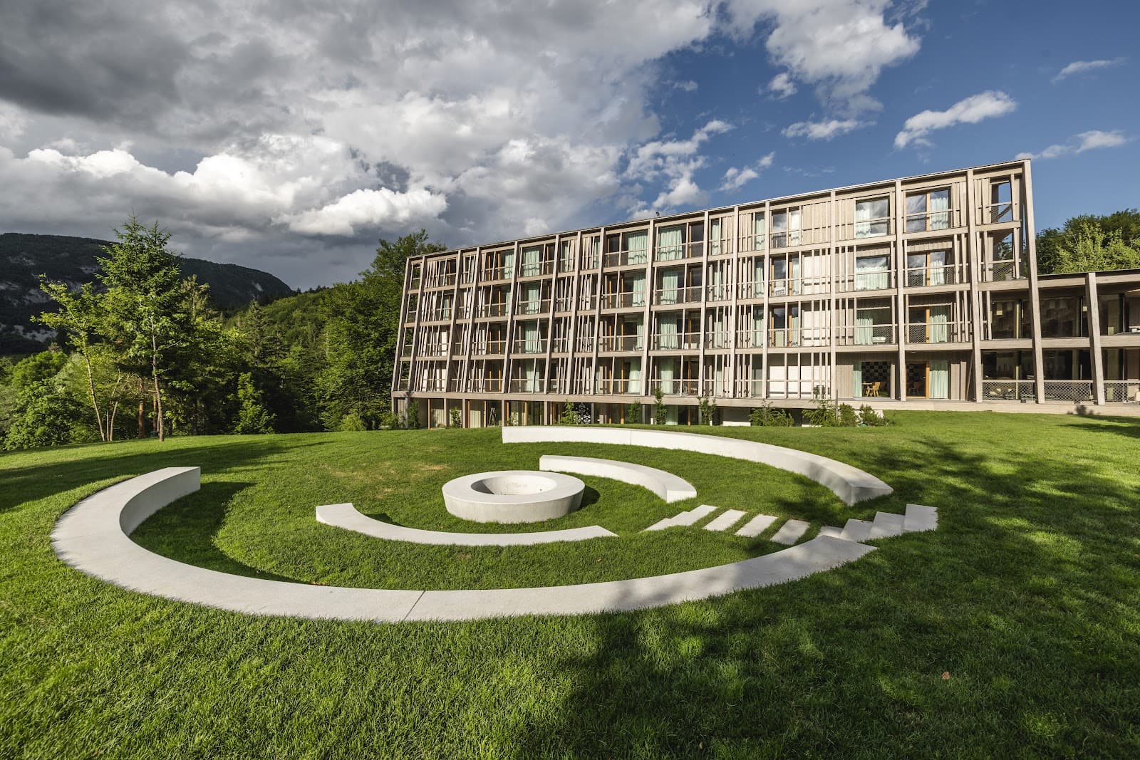 Modern hotel building with wood facade overlooking green lawn and mountains near Bohinj.