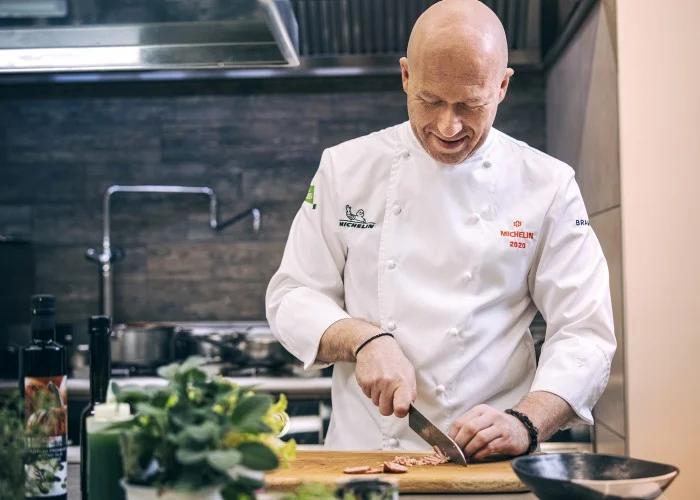 Chef in white coat chopping ingredients on wooden board during cooking class in kitchen