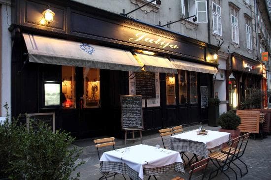 Outdoor dining tables set outside Julija restaurant with illuminated facade on a city street