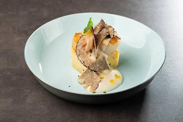 Seared scallop dish with shaved black truffle and white sauce on a pale blue plate.