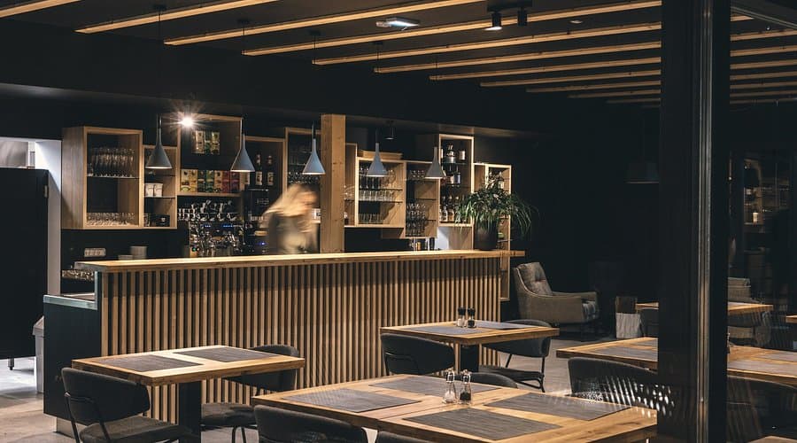 Modern restaurant interior with wooden bar, dark walls, and set dining tables at Restaurant Majerca Bohinj.