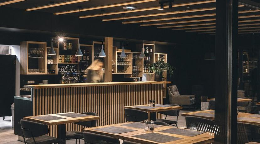 Modern restaurant interior with wooden bar, dark walls, and set dining tables at Restaurant Majerca Bohinj.
