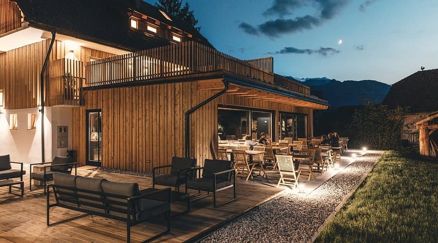 Illuminated wooden building with outdoor patio seating at dusk near mountains
