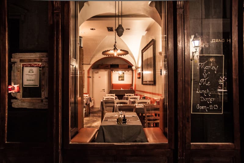 View into warmly lit restaurant interior with set tables through dark wooden doorway.