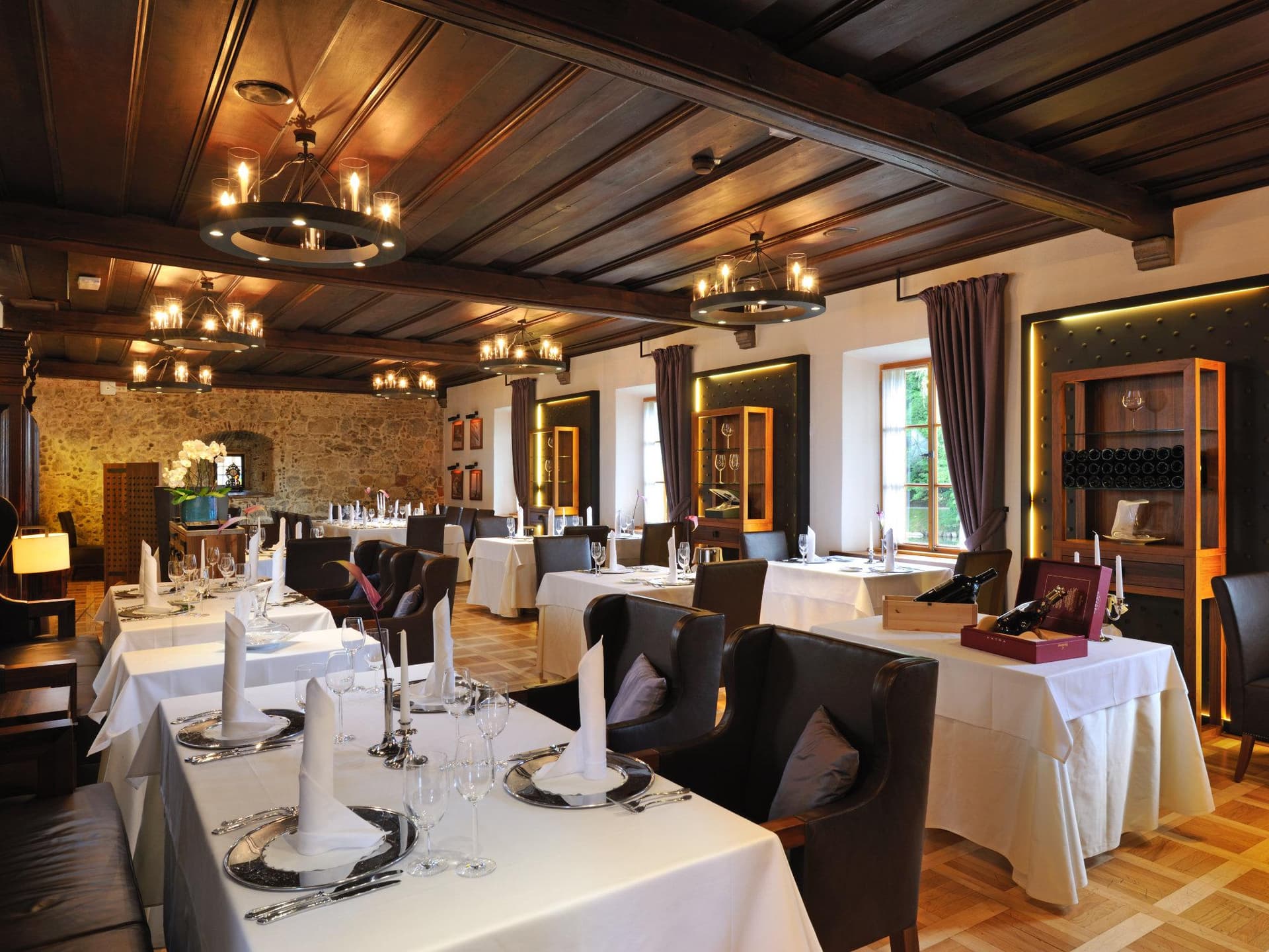 Dining room in Grad Otočec restaurant with white tablecloths, dark wood ceiling, and stone wall.