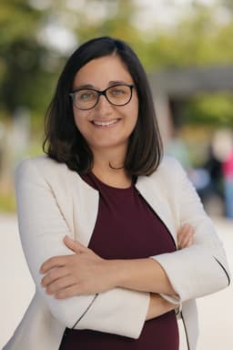 Portrait of a smiling woman with long dark hair against a solid gray background.