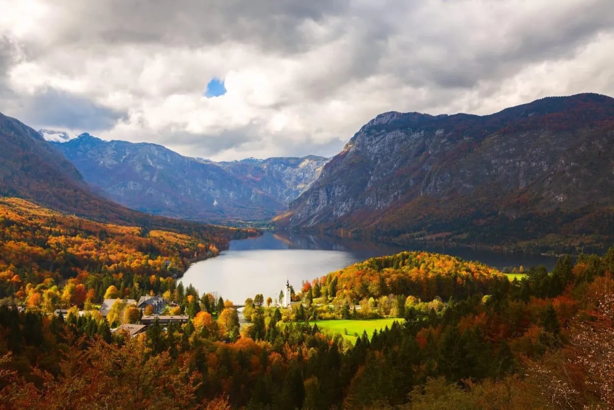 Lake Bohinj in Triglav National Park with autumn foliage and dramatic clouds.