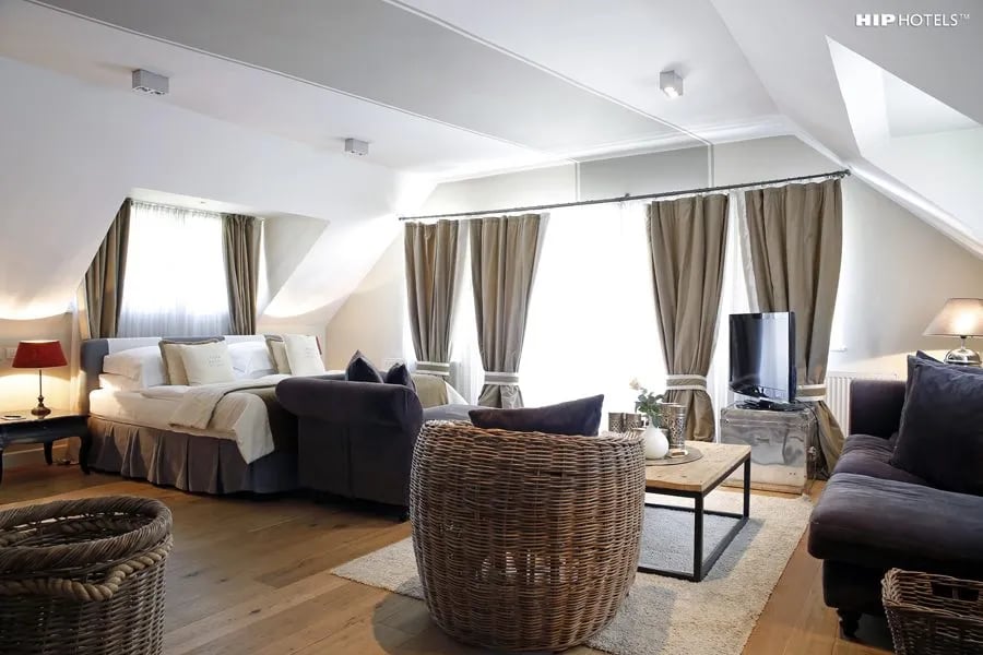 Attic hotel room with sloped ceiling, large bed, dark sofa, and wicker chair