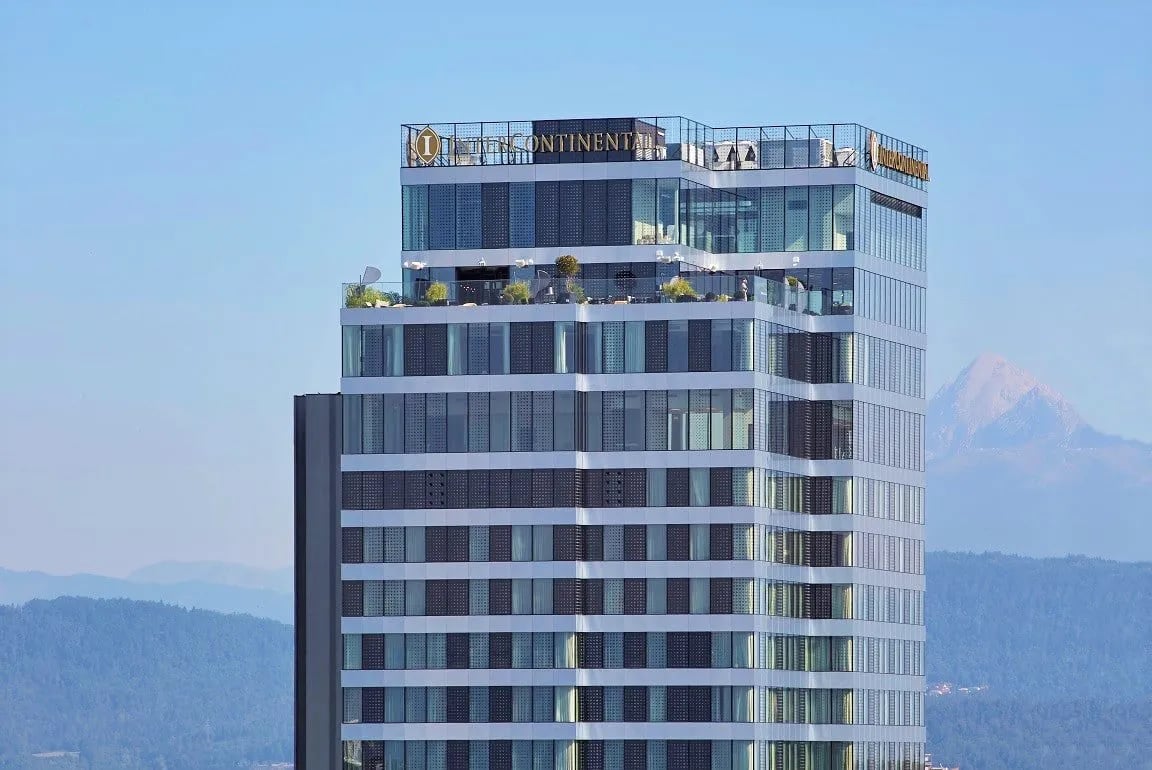 InterContinental Hotel skyscraper exterior with rooftop terrace against a backdrop of hazy mountains.