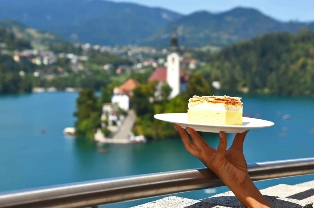 Cream cake held up with Lake Bled island and Julian Alps in background