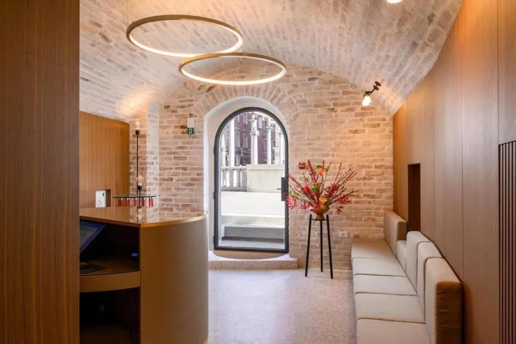 Hotel reception area with brick archway, modern lighting, and view of columns outside.