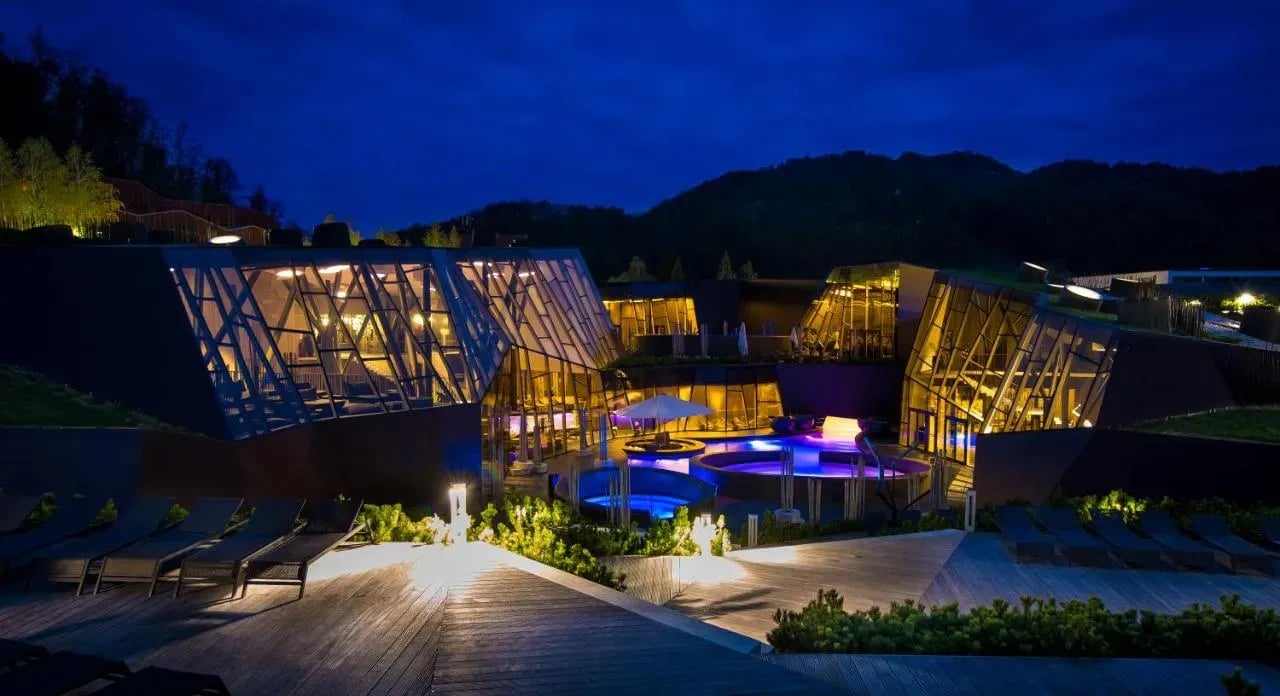 Modern spa complex with illuminated glass architecture and outdoor pools at night