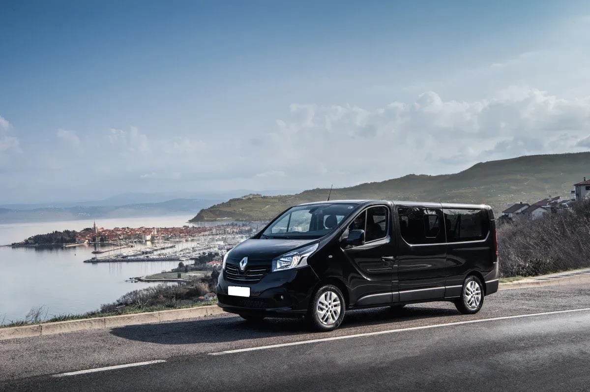 Black passenger van parked on road overlooking coastal town and marina