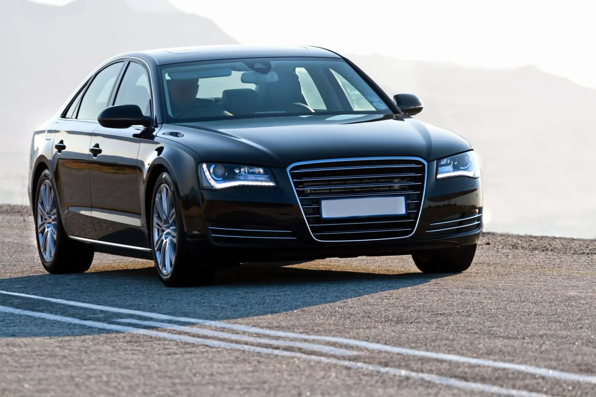 Black luxury sedan driving on asphalt road with distant hazy mountains