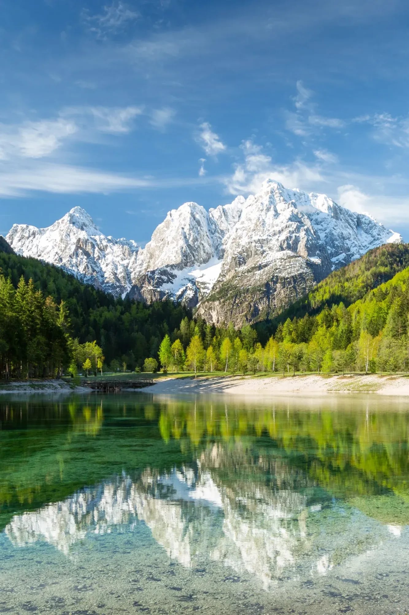 Jasna Lake with snow-capped mountains reflected in clear green water and surrounding forest