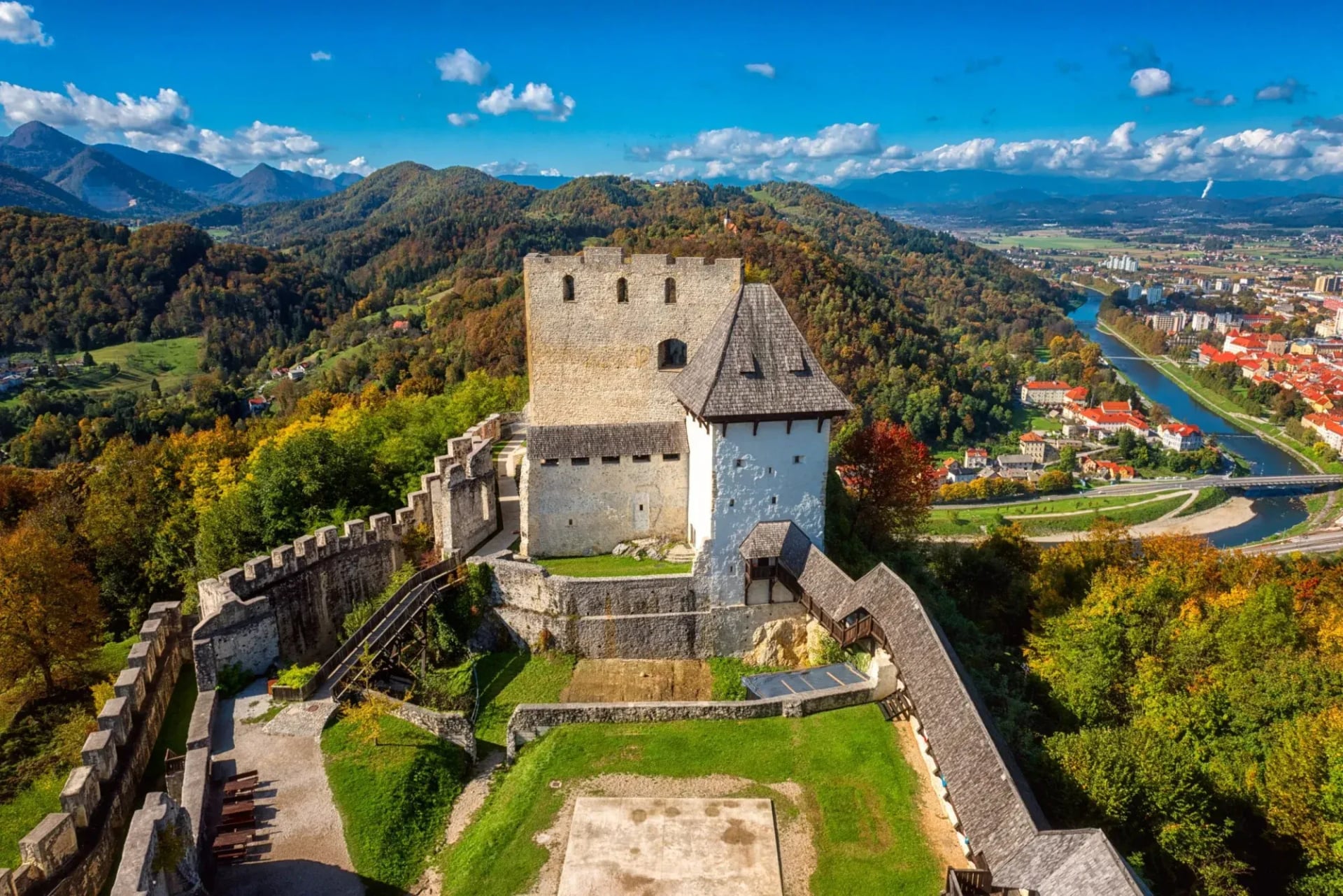 Celje Castle overlooking the city and river valley with autumn foliage and mountains.