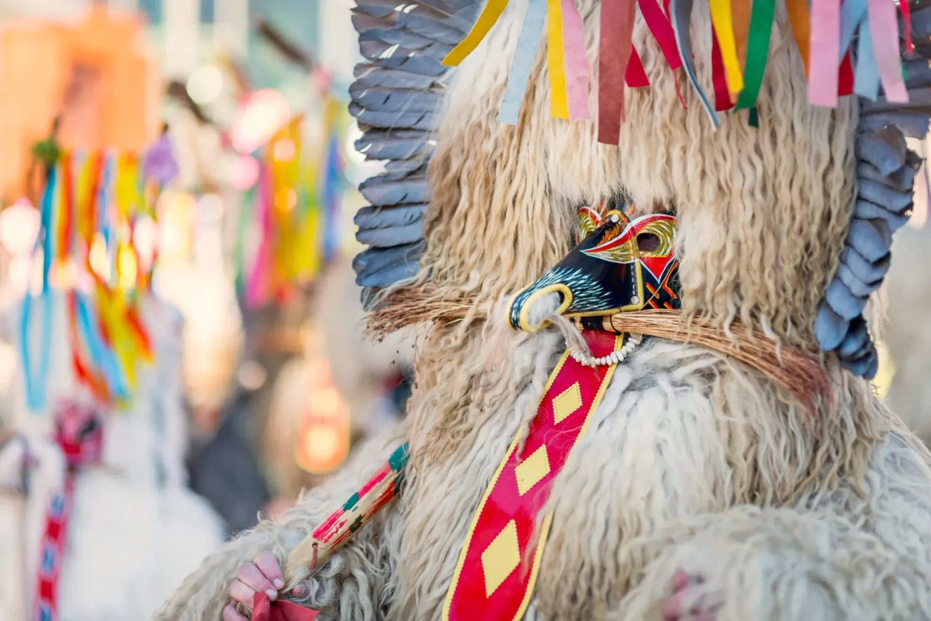 Kurent figure in traditional costume with mask and colorful ribbons during a carnival celebration.