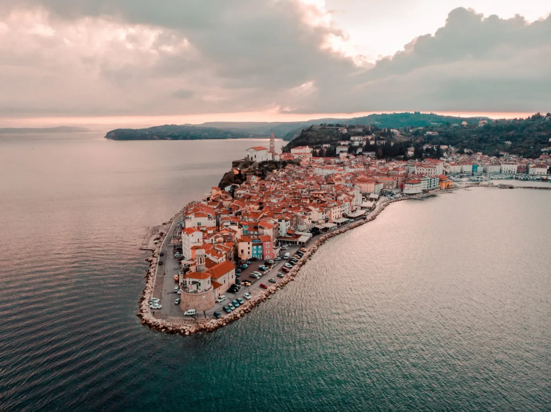 Aerial view of Piran peninsula town with terracotta roofs on the Adriatic Sea at sunset.