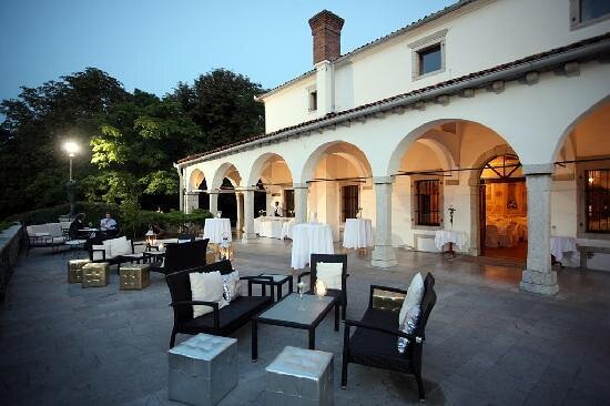 Outdoor terrace event setup with seating and arched white building at dusk