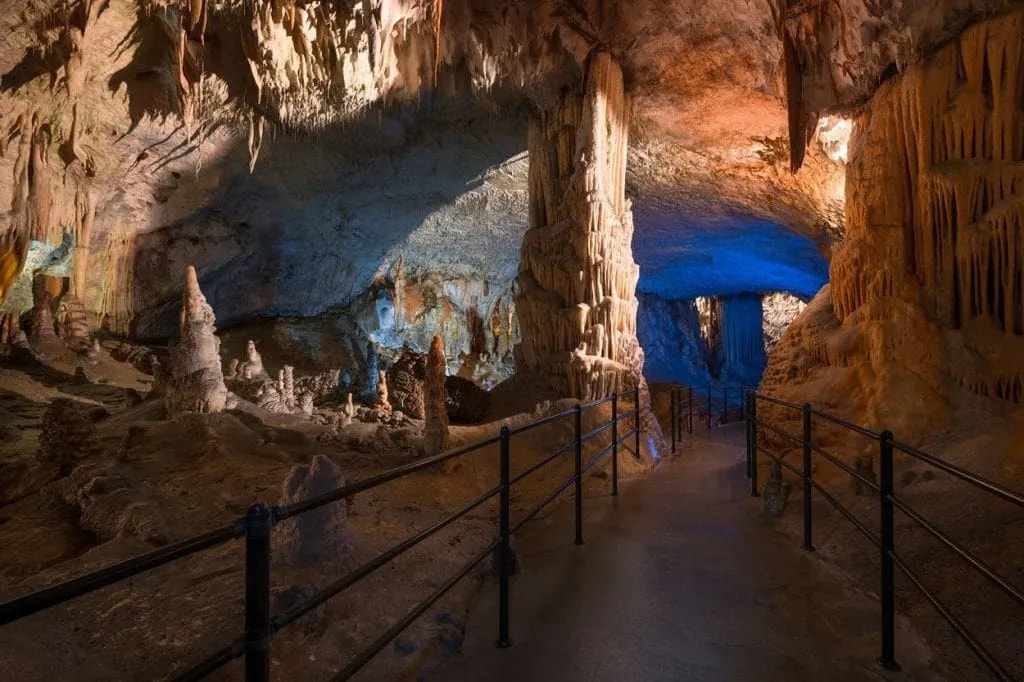 Postojna Cave interior with illuminated stalactites, stalagmites, and a marked pathway.