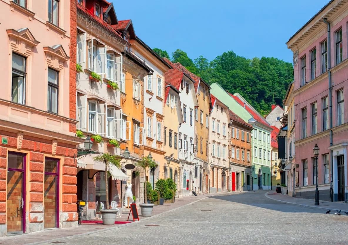 Cobblestone street lined with colorful historic buildings leading toward a green hillside in Gornji trg, Ljubljana.