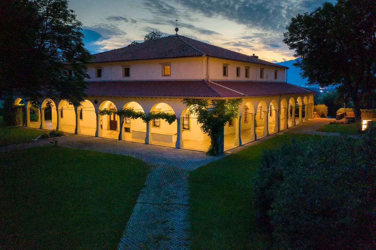 Illuminated villa with arched portico and tiled roof at dusk, Dvorec Zemono grounds
