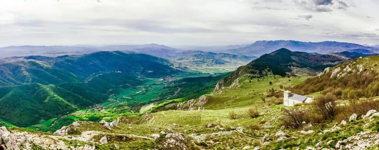 Panoramic view of green mountains and valleys in Vipava Valley, Slovenia, with a small white building.