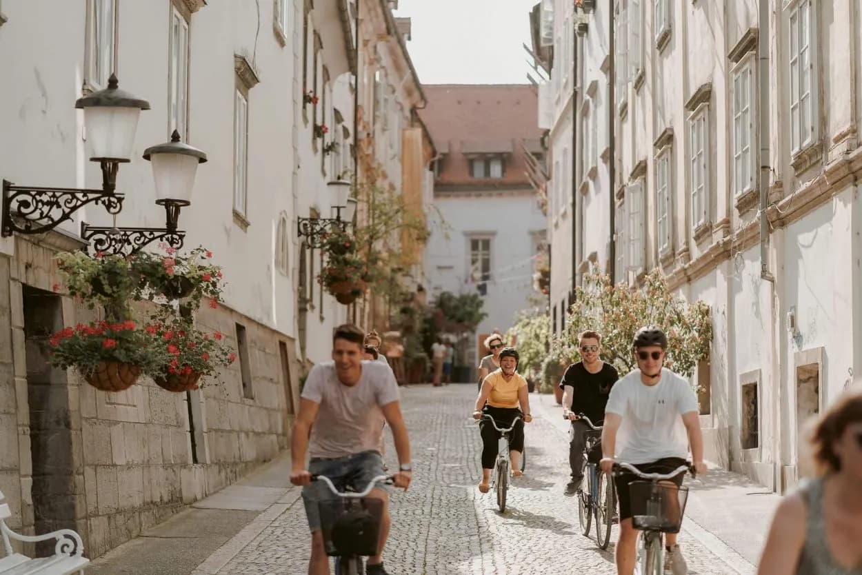 Cycling tour group on cobblestone street in Ljubljana with historic buildings and flower baskets.