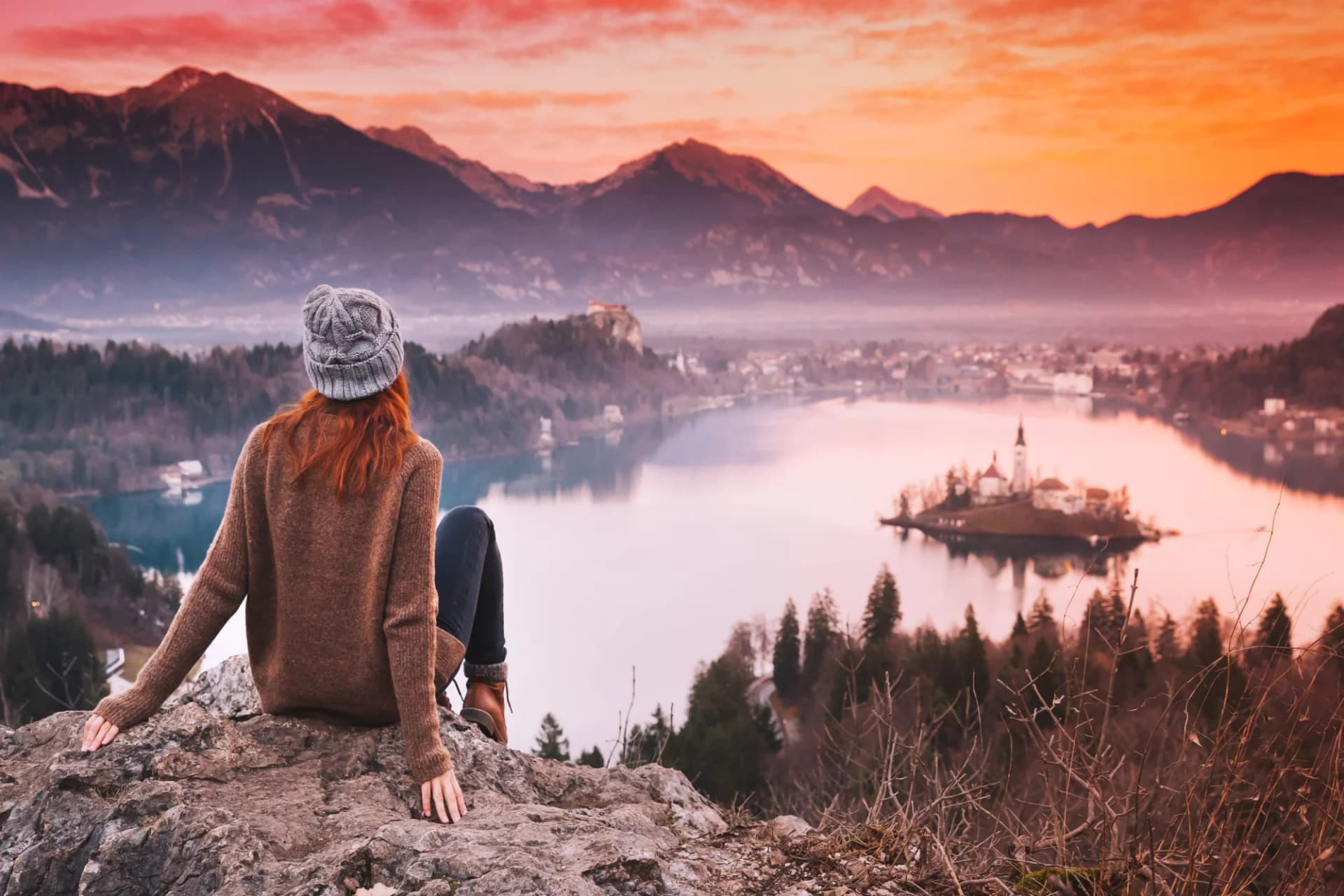 Woman looking over Lake Bled island church and mountains at sunset in Slovenia