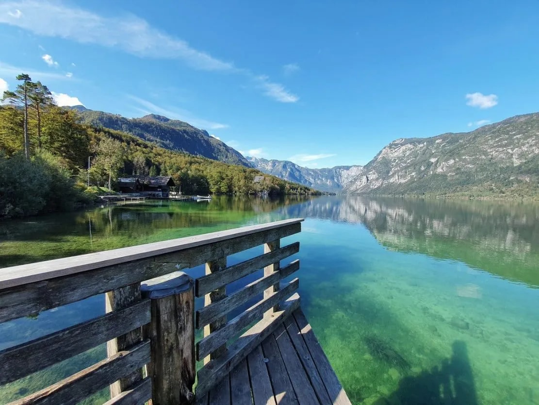 Wooden pier overlooking clear turquoise water of Bohinj Lake with mountains in background.