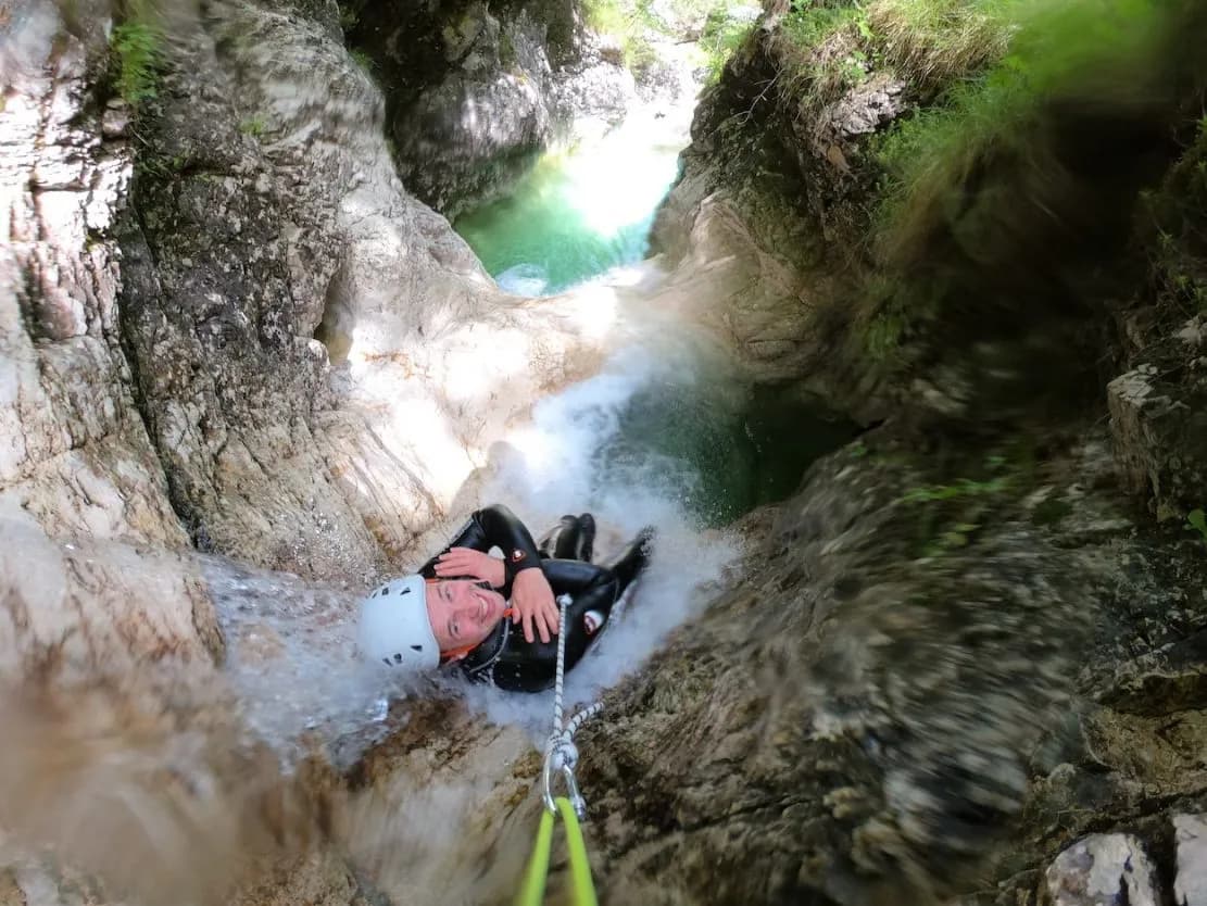 Canyoning down a waterfall in a rocky gorge with turquoise pools, Soca.