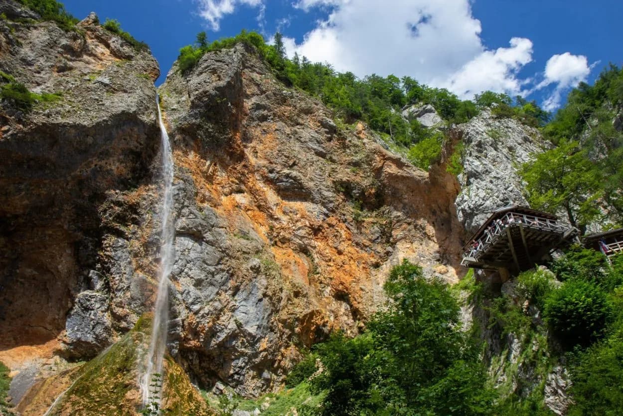Waterfall cascading down a rocky gorge with a wooden viewing platform built into the cliff face.