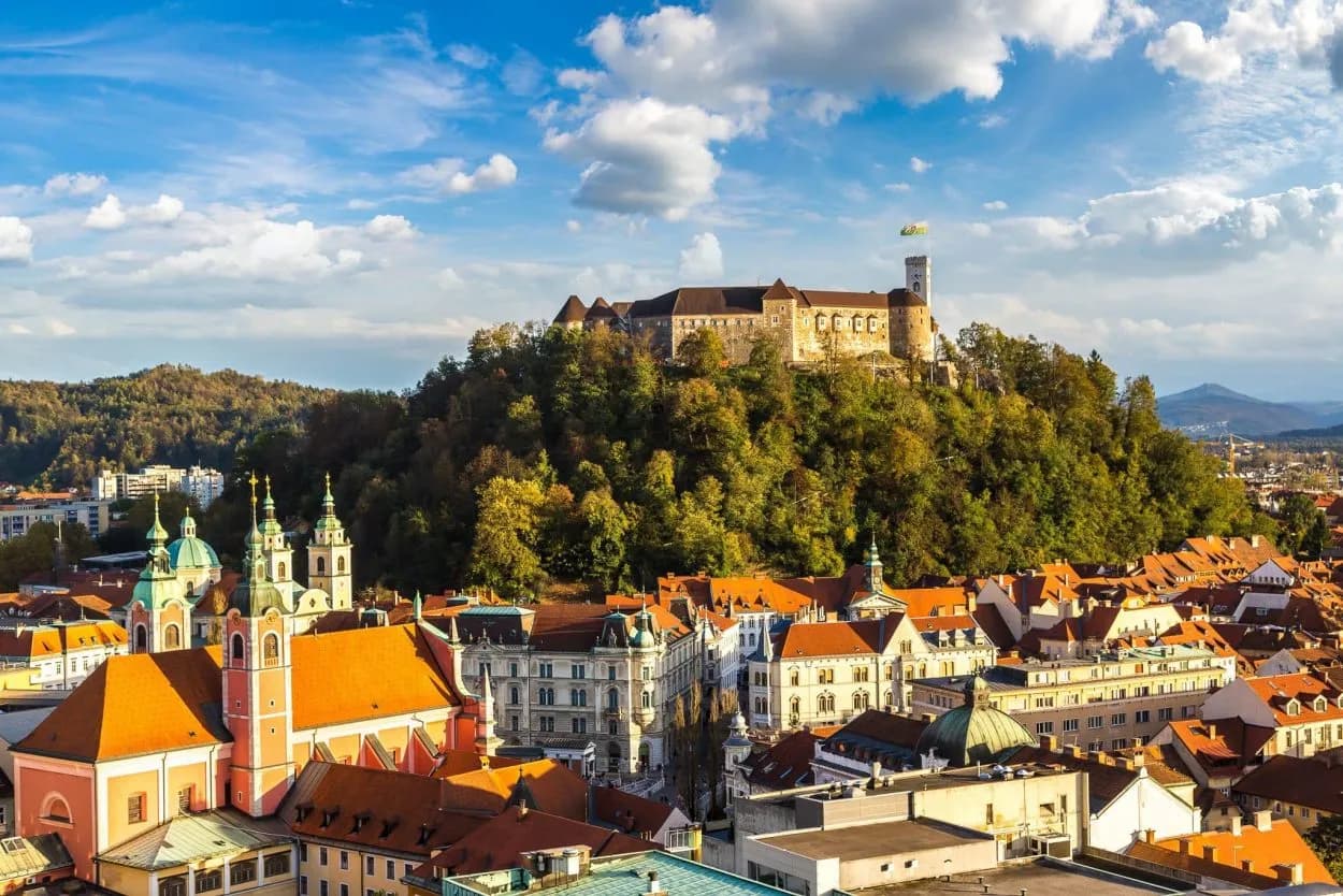 Ljubljana Castle overlooks the city's terracotta rooftops and green church domes under a blue sky.