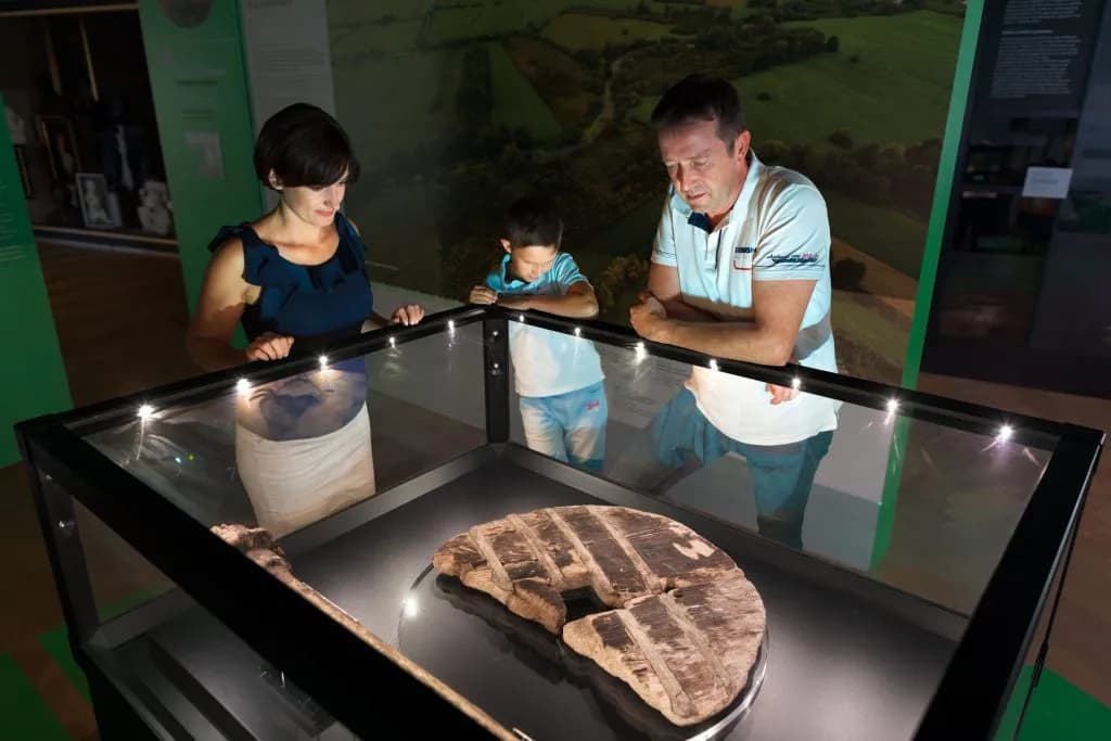 Family viewing the oldest wooden wheel exhibit in a display case at Ljubljana City Museum.
