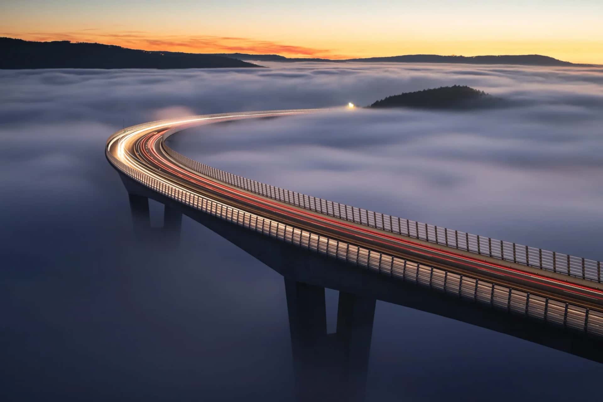 Highway viaduct above thick fog at sunrise with vehicle light trails near Crni Kal.