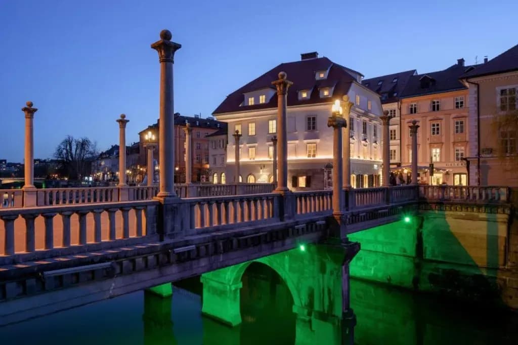 Triple Bridge with stone columns illuminated at night over river in Ljubljana