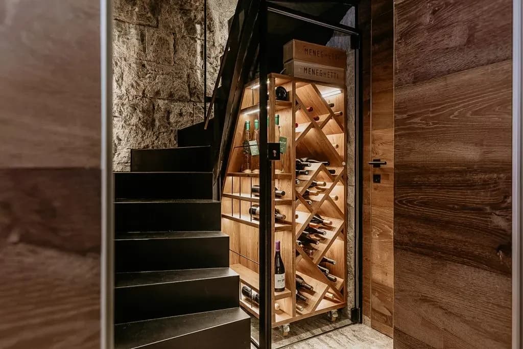 Illuminated wooden wine rack stored under dark staircase beside stone wall